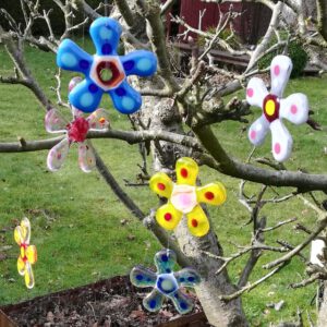 Bunte Blumen aus Glas zum Aufhängen, die alsGartendekoration in Handarbeit per Glasfusing hergestellt wurden.